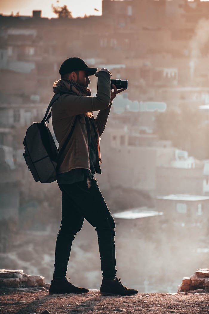 A photographer in a jacket capturing a city view with a DSLR during sunset.