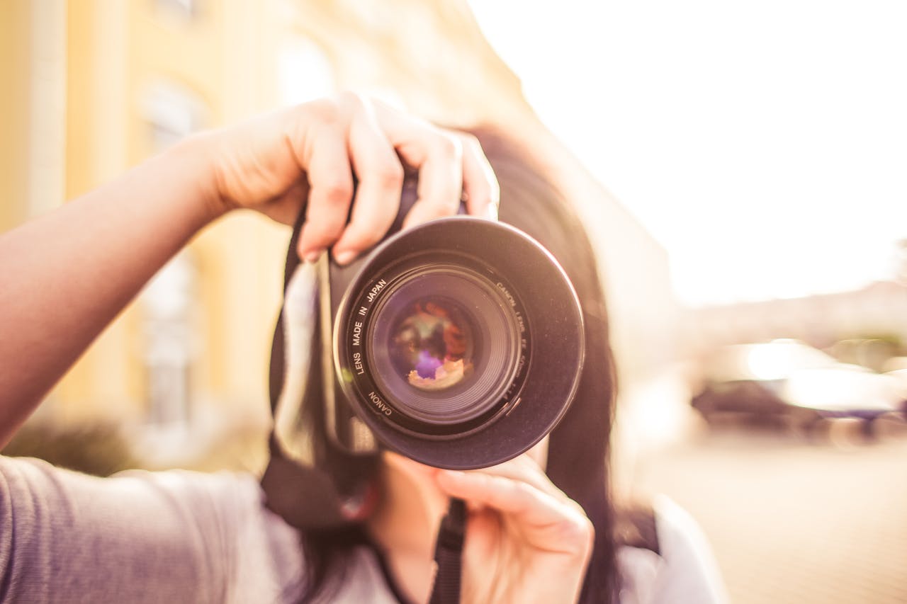 Mastering the First Impression: Your intriguing post title goes here A young woman photographer focuses through a DSLR camera lens outdoors in bright daylight.