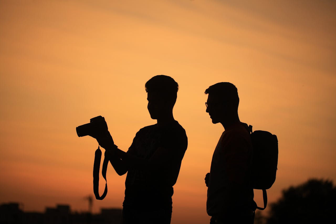 my-qualifications Two photographers silhouetted against a warm sunset sky, capturing serene moments.